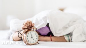 کھڑکی سے صبح کی روشنی میں جاگتی ہوئی عورت، بستر کے قریب