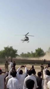 سرکاری ہیلی کاپٹر کے قریب جمع افراد اور پوسٹرز دکھاتا منظر
